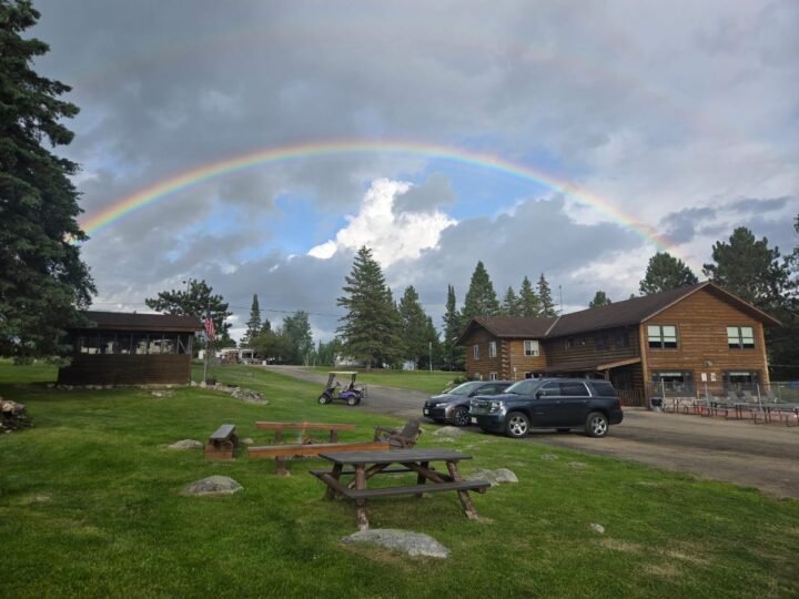 Rainbow arching over rustic log cabin resort with picnic tables