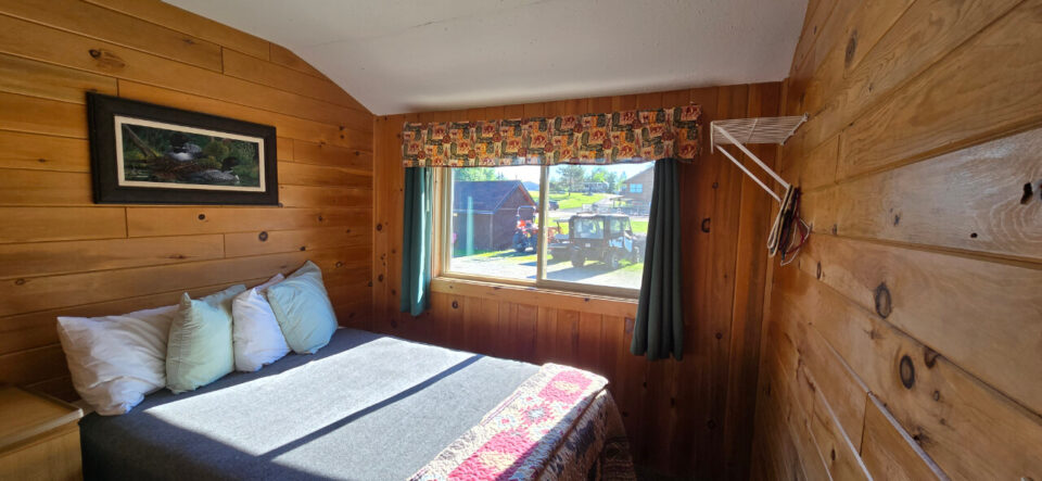 Cozy rustic cabin bedroom with wood paneling and window view