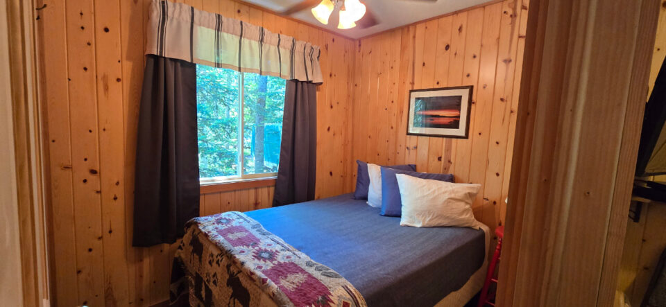 Cozy rustic cabin bedroom with knotty pine walls and nature view