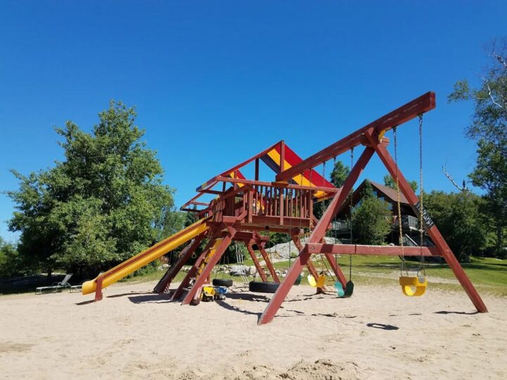 Colorful wooden playground with slide and swings on sandy ground