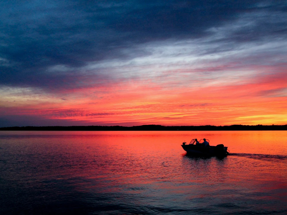 Silhouetted boat cruising on lake during vivid red sunset