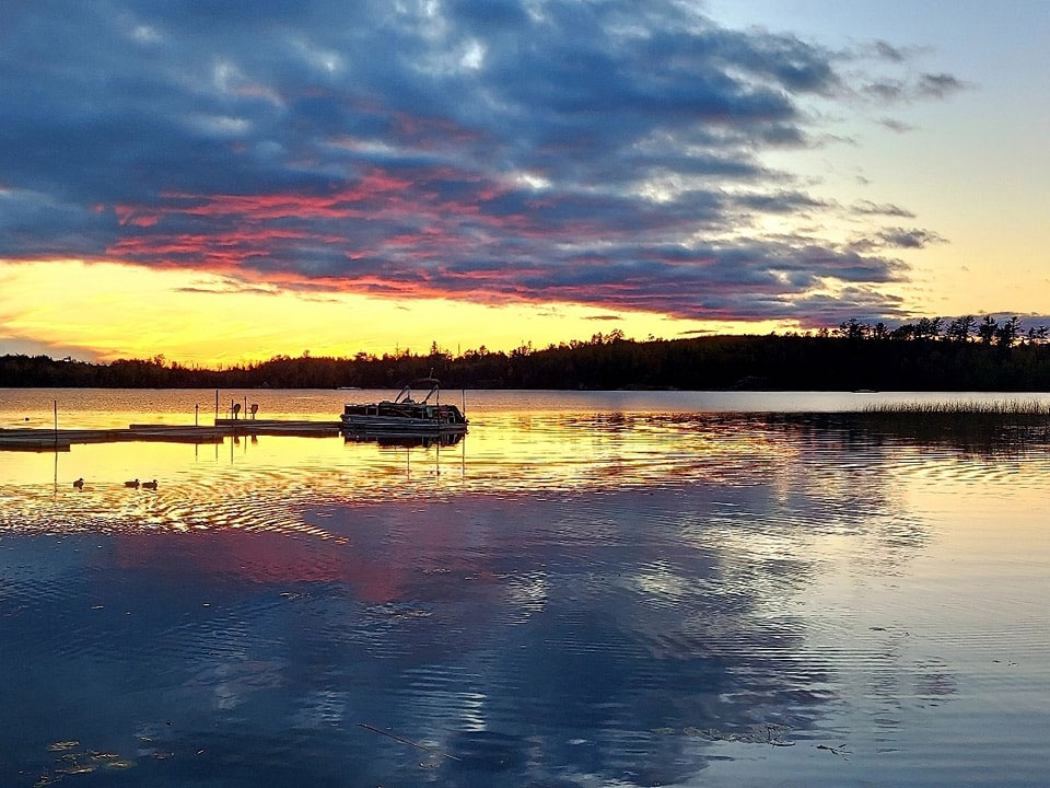 Vibrant sunset over calm lake with docked pontoon boat